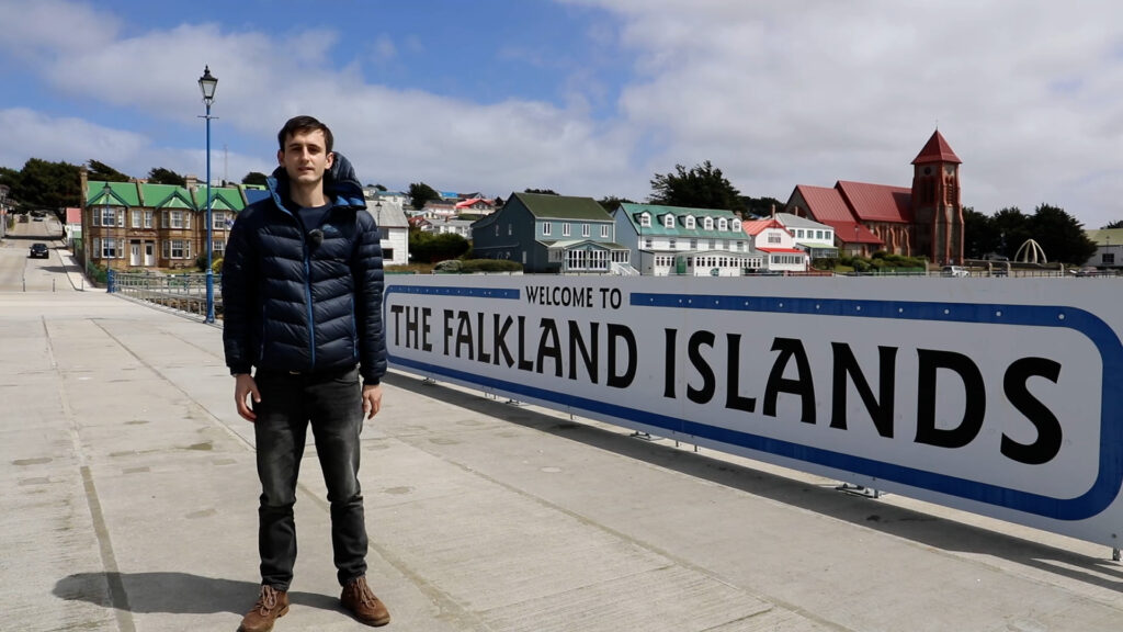 Charles standing next to the 'Falkland Islands' sign on the public jetty in Stanley